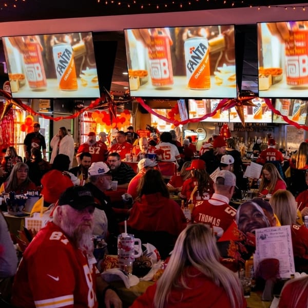 A crowded sports bar with patrons in red jerseys watching a game on multiple large screens.
