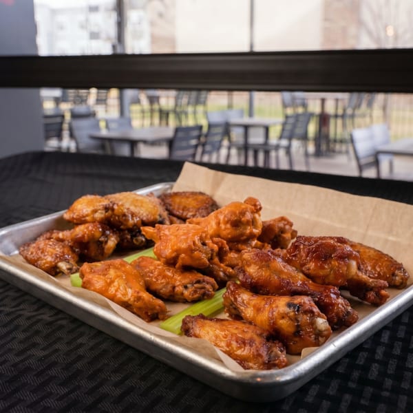 A metal tray filled with saucy chicken wings and celery sticks, with an outdoor patio in the background.