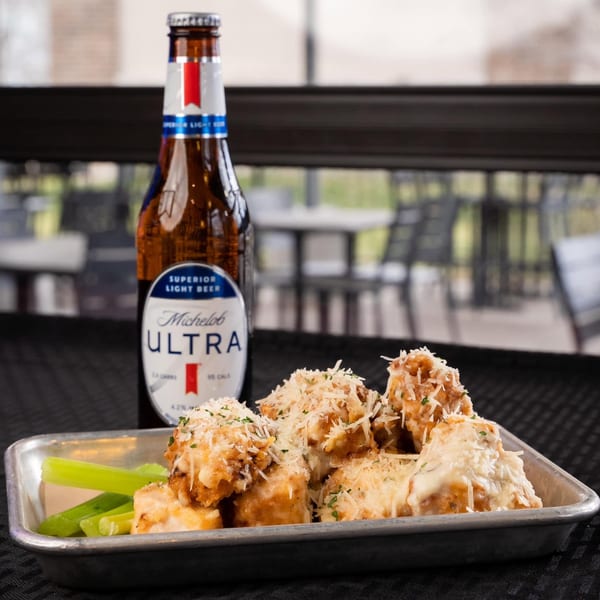A bottle of Michelob Ultra beer next to a tray of cheesy chicken wings and celery sticks.