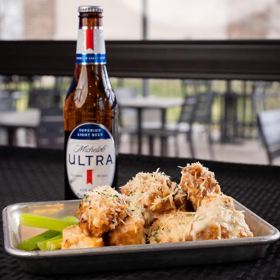 A bottle of Michelob Ultra beer next to a tray of cheesy chicken wings and celery sticks.