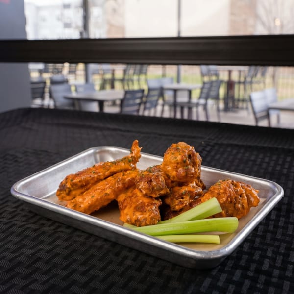 Buffalo wings and celery sticks on a metal tray, with an outdoor patio in the background.